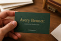Hand holding a personalized bottle-green Avery Bennett business card with a raised gold-foil name