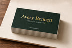 Stack of personalized bottle-green business cards with raised gold-foil names and natural white edges