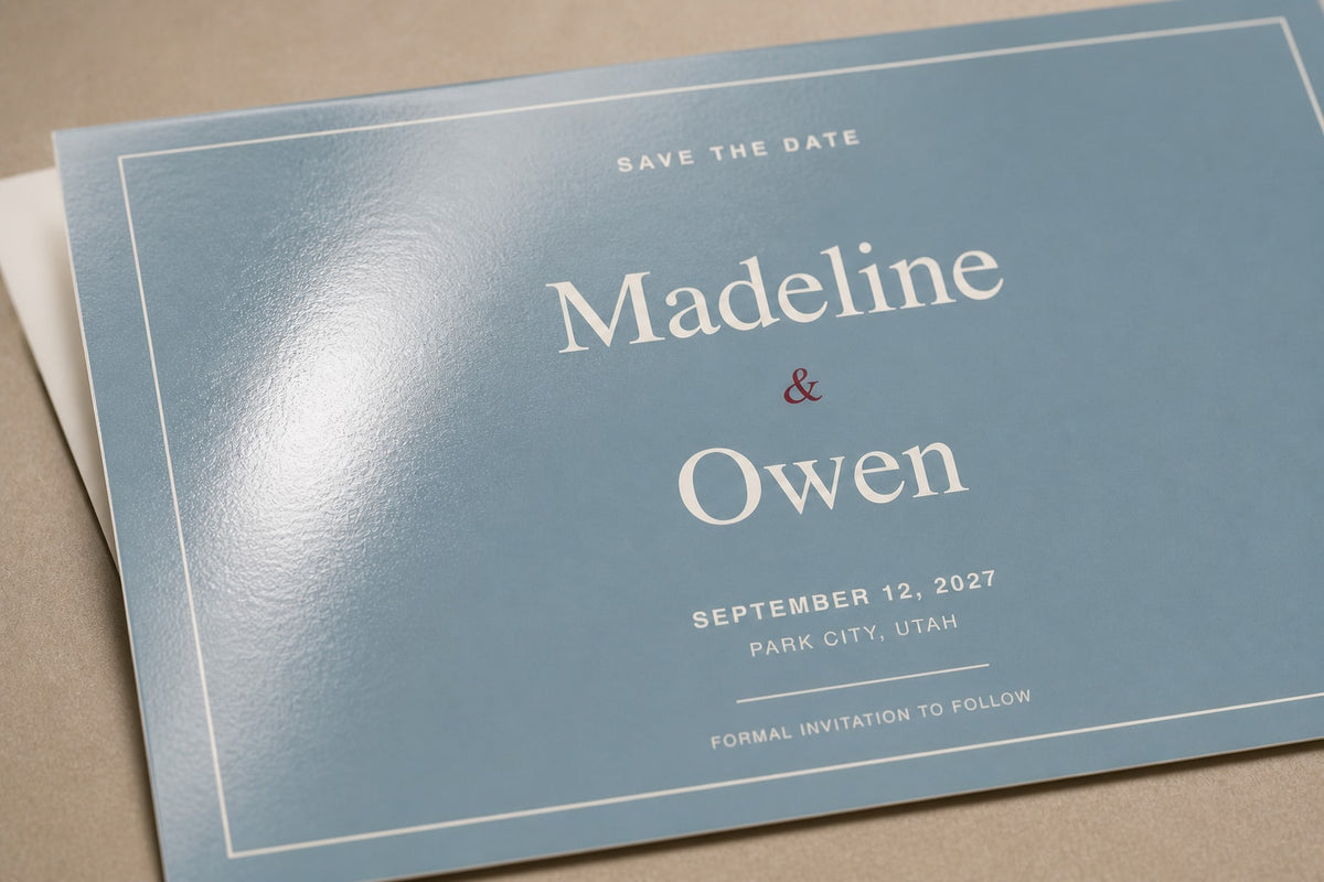 Macro close-up of the Madeline and Owen postcard showing a broad reflection across the glossy blue front